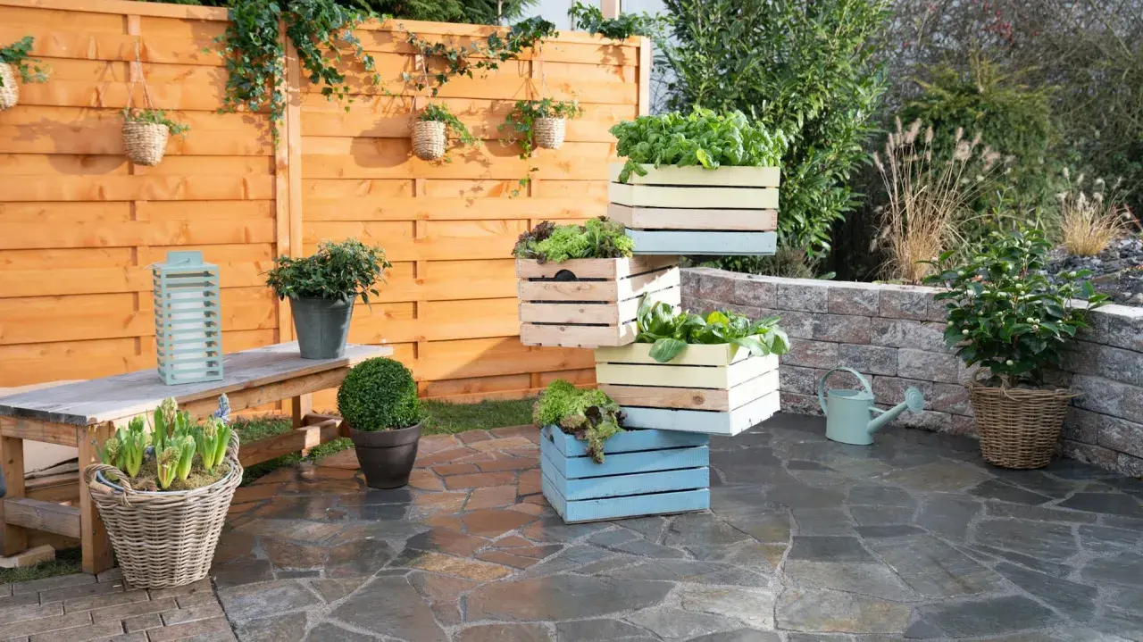 Fioriera fai da te con cassette di legno colorate, piene di verdure fresche, su un patio in pietra.