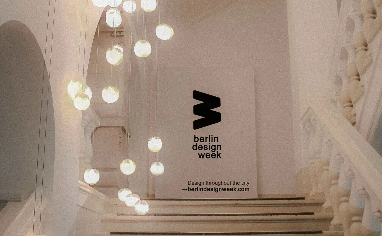 Eine Treppe mit Hängeleuchten und einem Banner für die **Berlin Design Week**.