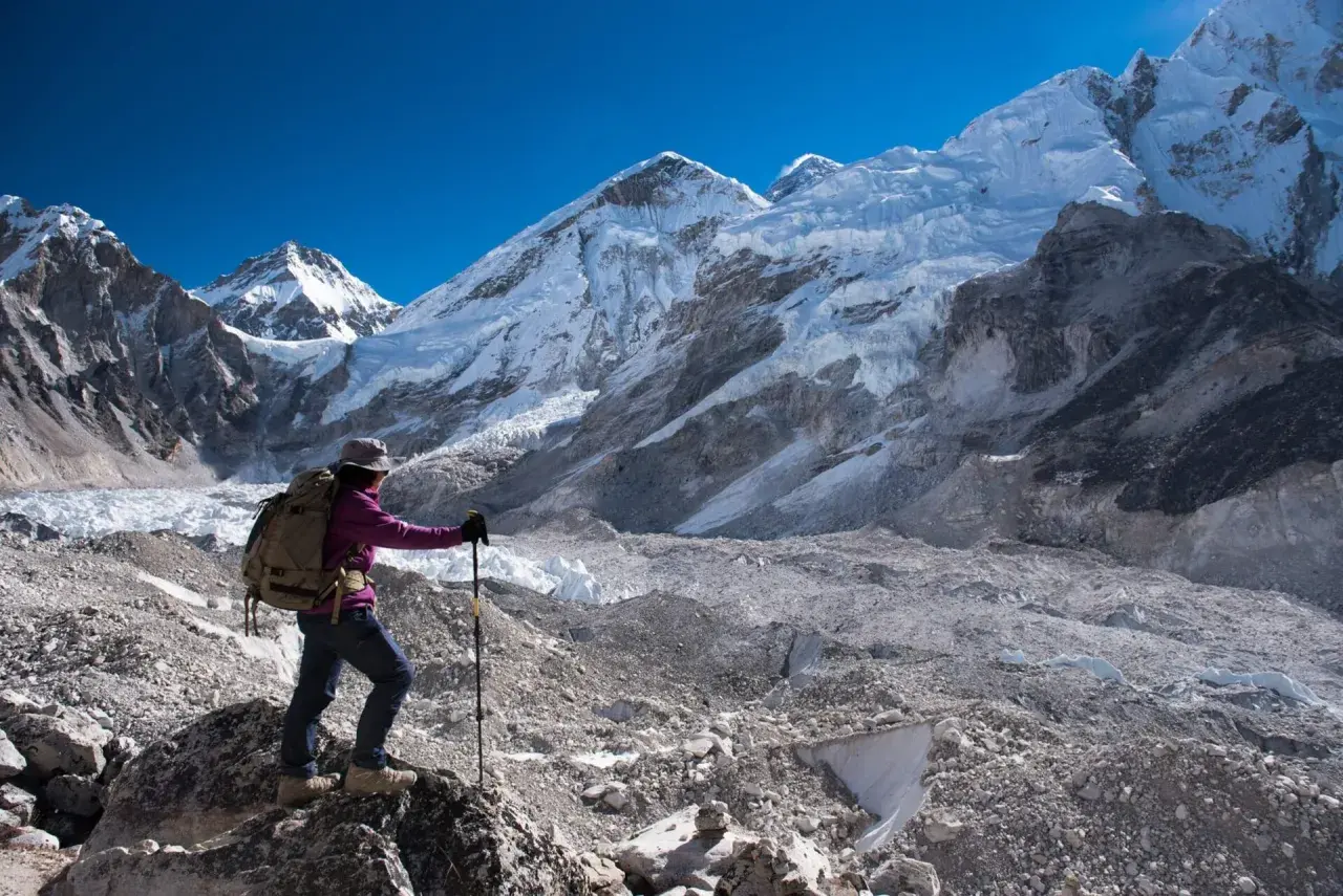 Turystka z plecakiem i kijkami trekkingowymi podziwia majestatyczne szczyty Himalajów w okolicy **Mount Everest Base Camp**.