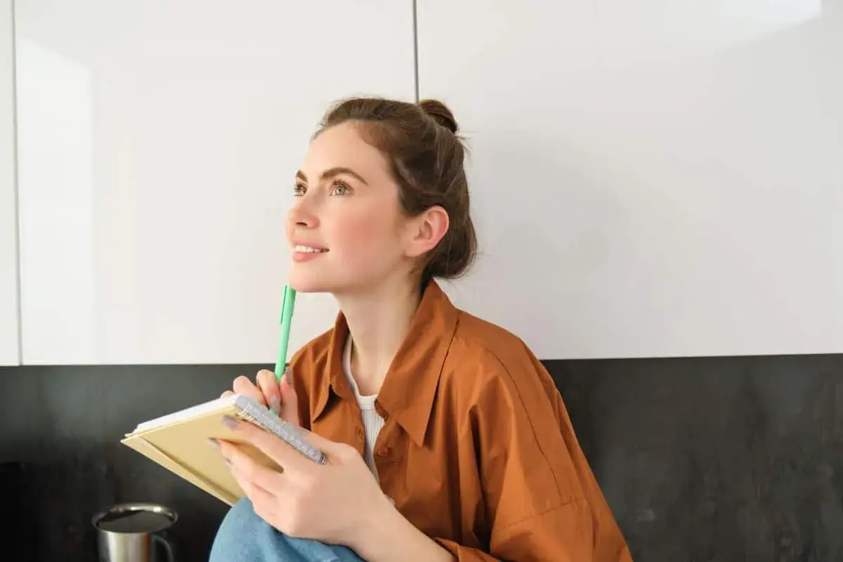 Ragazza pensosa, con un quaderno e una penna, dallo sguardo sognante. Una persona curiosa e operosa.