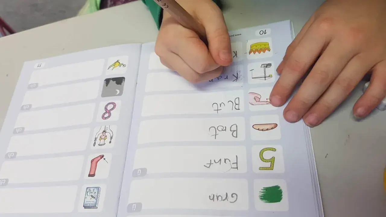 Kind schreibt im Rahmen des Förderunterrichts Grundschule Wörter wie "Kran" und "Brot" in ein Übungsheft.