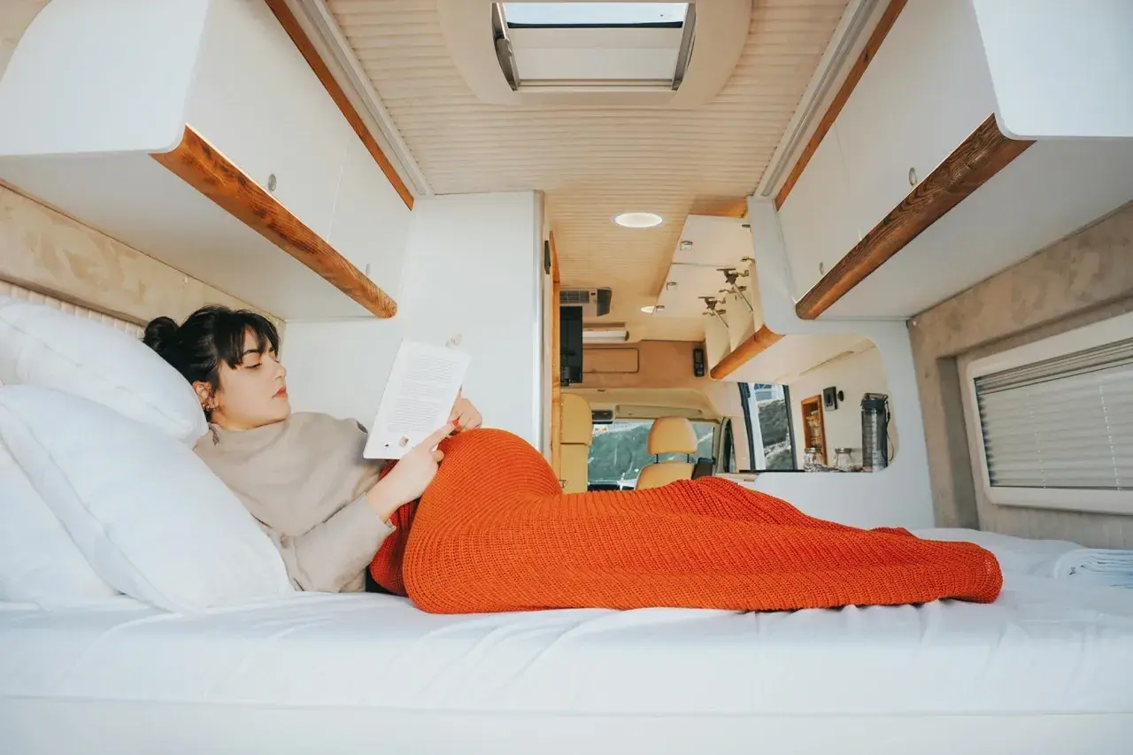 Une femme lit un livre, confortablement installée dans son camping-car fraîchement rénové. L'espace est lumineux et moderne.