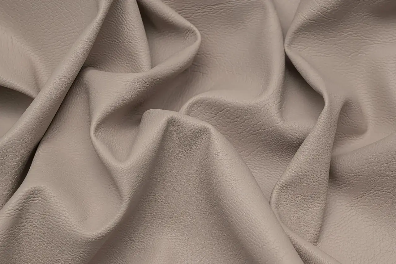 Miękka, beżowa eko skóra z delikatną fakturą, pofałdowana tworząc eleganckie draperie.
