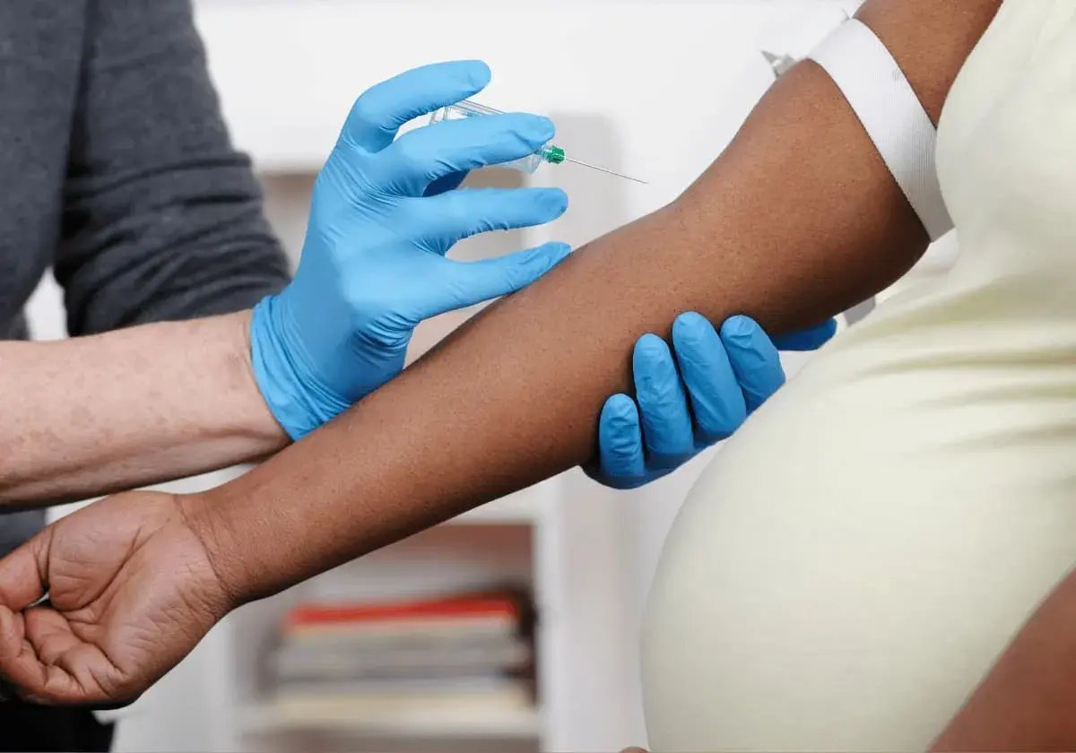 Blodprov tas för nipt test vecka 10. En hand med blå handske håller armen medan en annan hand med blå handske för in en nål.