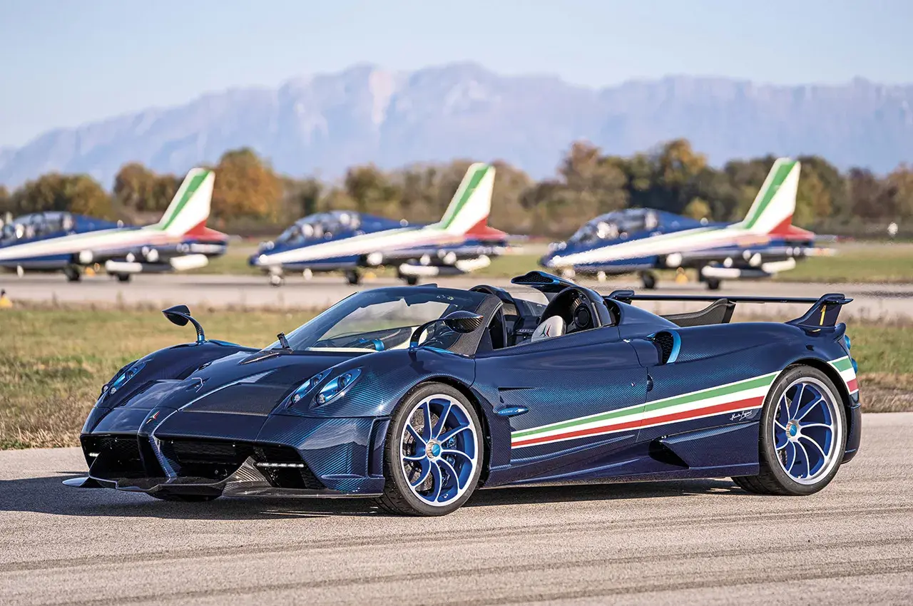 Niebieski Pagani Huayra Roadster z włoską flagą na boku, obok samolotów akrobacyjnych. Jego pagani huayra cena jest astronomiczna.