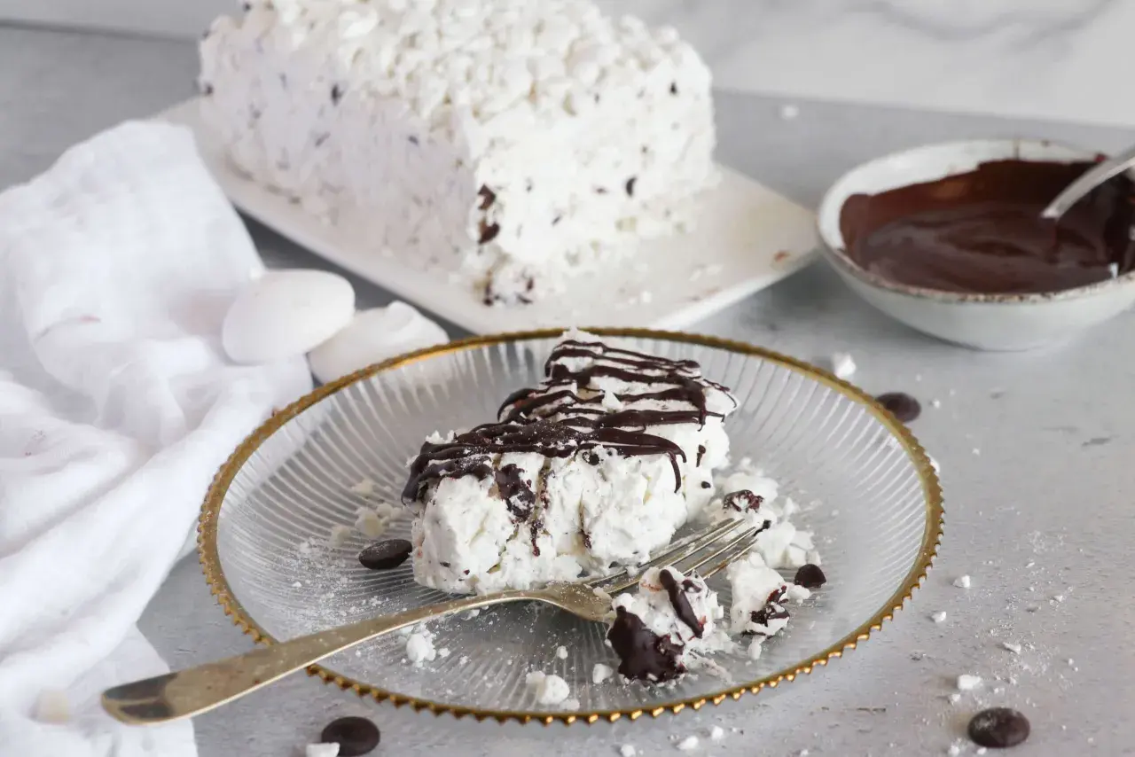 Una fetta di meringata al cioccolato, soffice e golosa, con scaglie di cioccolato e una cascata di salsa al cacao.