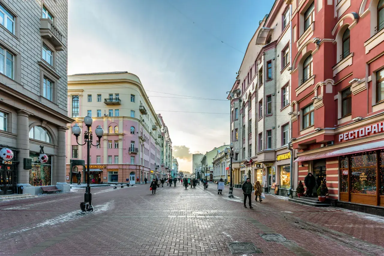 Zimowy spacer po Arbat w Moskwie. Ludzie przechadzają się brukowaną ulicą między kolorowymi kamienicami, a w oknach sklepów migoczą świąteczne dekoracje.