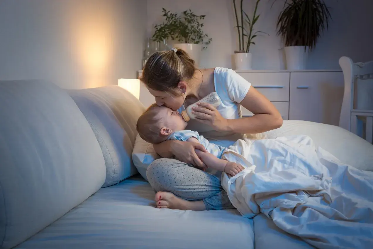 Matka karmi dziecko butelką w łóżku, czule całując je w czoło. Nawet koszmary senne nie są straszne, gdy czuwa kochająca mama.
