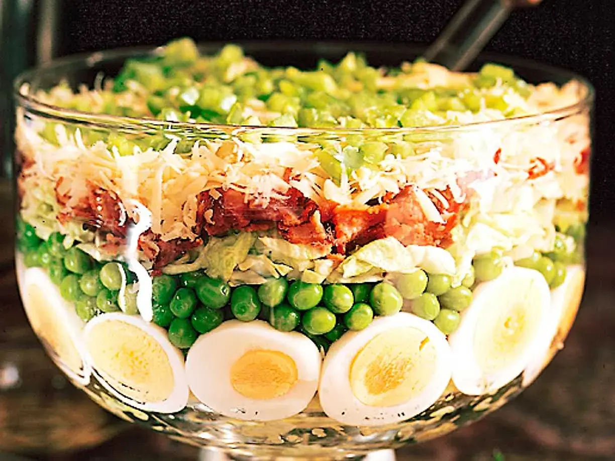 Lager på lager i en glasskål: ägg, gröna ärtor, sallad, bacon, ost och paprika. Ett härligt sallad recept!
