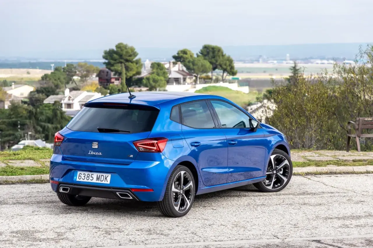 Un Seat Ibiza 1.2 gasolina, azul brillante, aparcado en un paisaje con casas y árboles. Opiniones sobre su diseño y rendimiento.