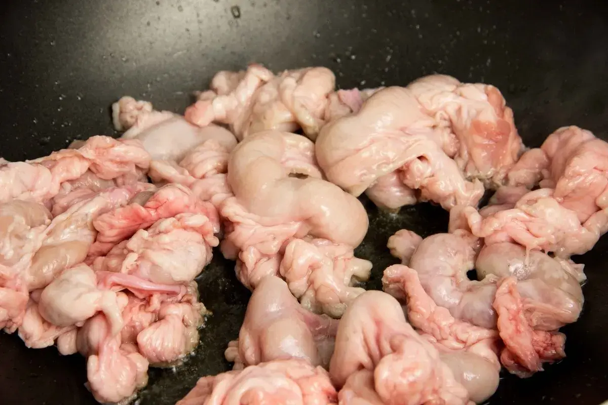 Unos gallinejas y entresijos crudos se cocinan en una sartén negra, listos para ser un plato tradicional.