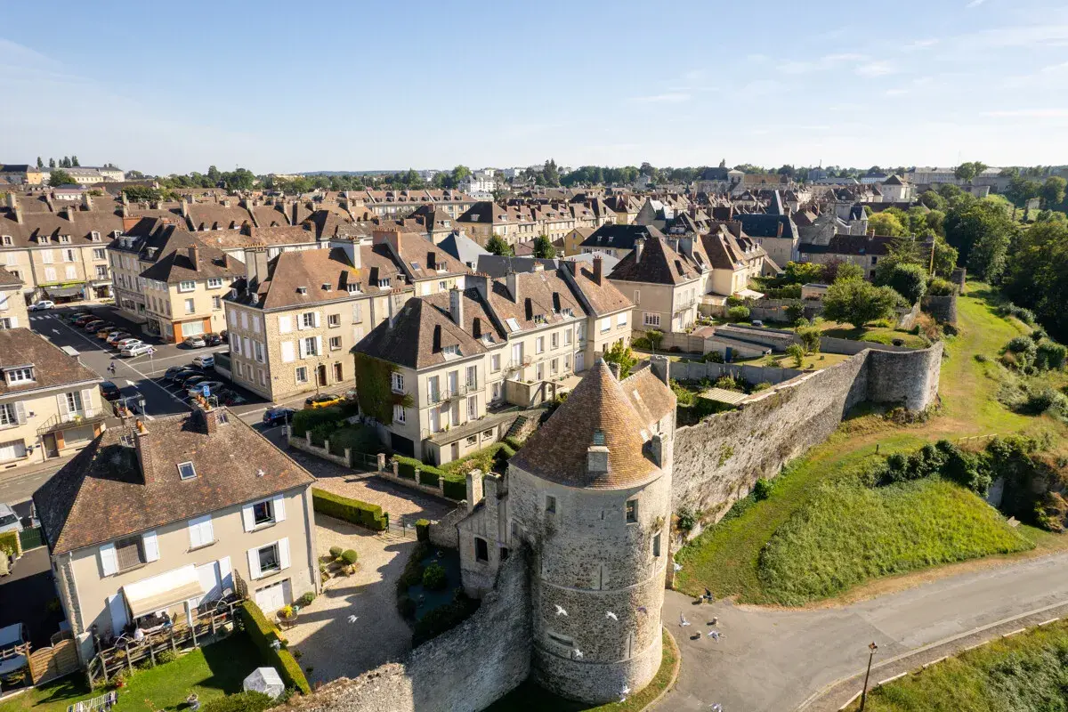Vue aérienne d'une ville fortifiée de la Suisse Normande, avec ses toits en ardoise, ses maisons en pierre et sa tour médiévale.