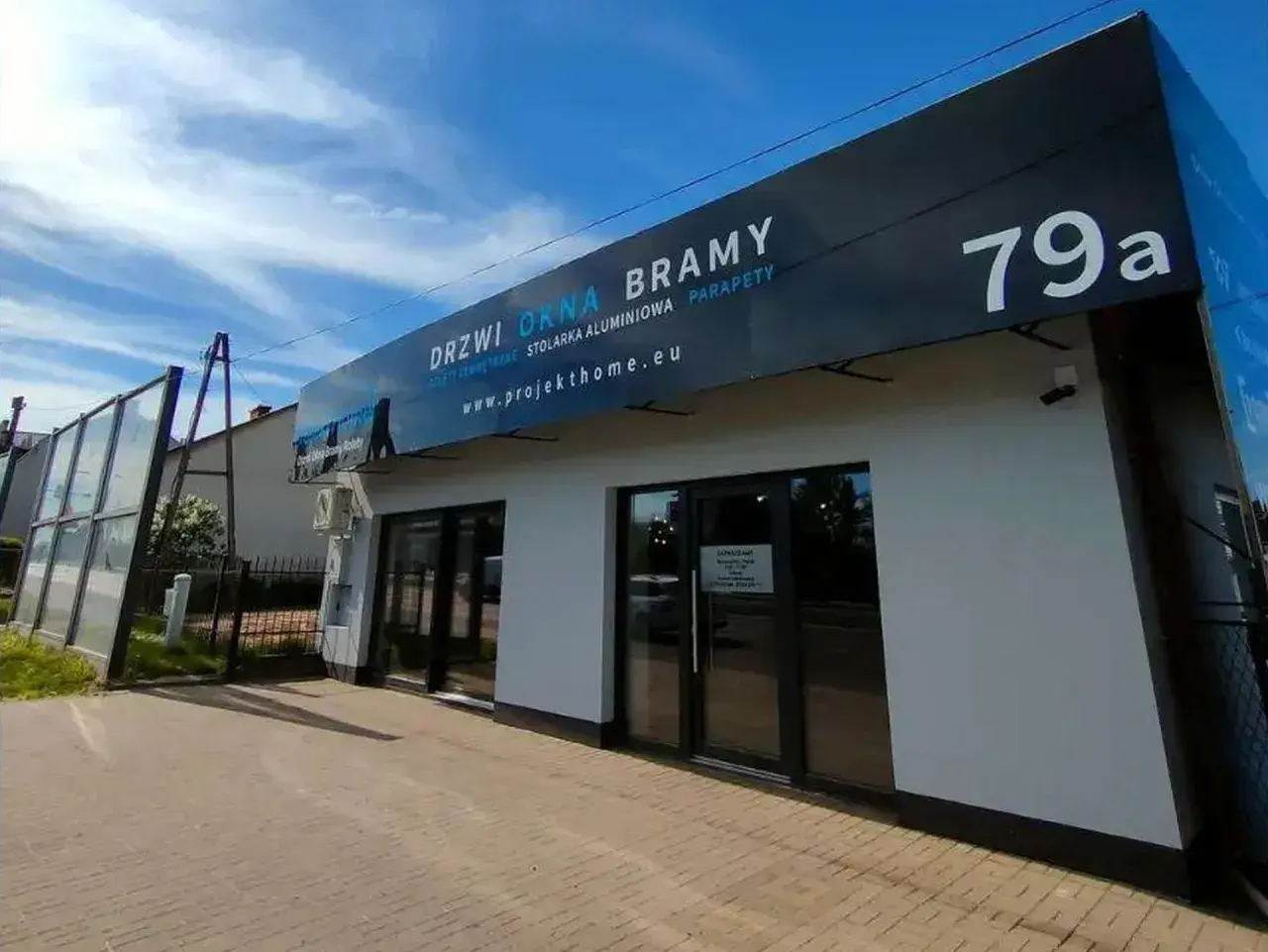 Nowoczesny salon okien i drzwi z szyldem "DRZWI OKNA BRAMY" i numerem 79a.