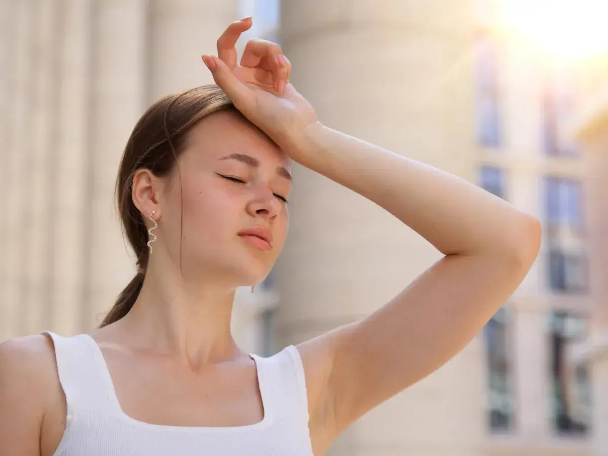 Une jeune femme essuie sa sueur sous un soleil de plomb, se demandant combien de temps dure un coup de chaleur.