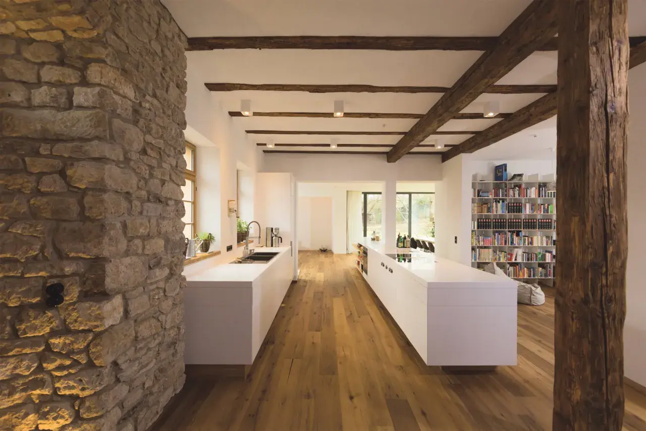 Modernes Wohnen mit Fachwerk: Eine Küche mit weißen Inseln und Holzbalken, die das Fachwerk innen gestalten.