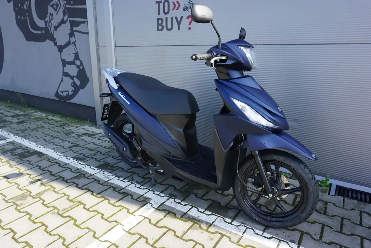 Elegancki, granatowy skuter Suzuki Address 110 zaparkowany na kostce brukowej.