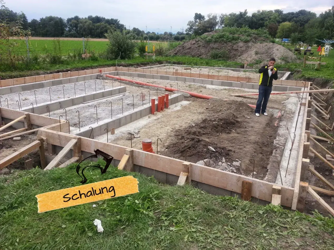 Baufortschritt: Die **Schalung** für das Fundament ist vorbereitet, Bewehrungsstahl und Rohre liegen bereit.