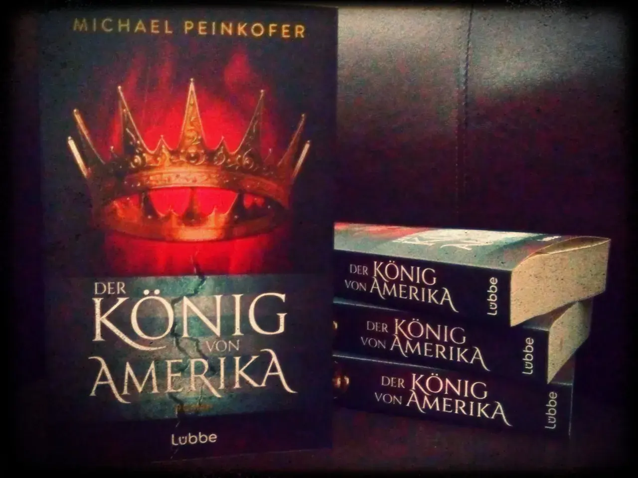 Michael Peinkofer präsentiert "Der König von Amerika". Ein Buchcover mit Krone und gestapelte Exemplare des Romans.