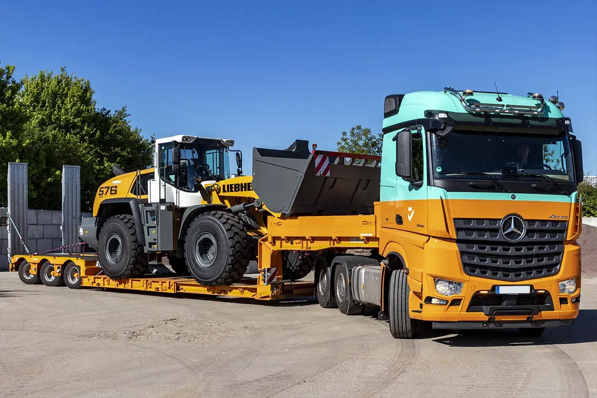 Pomarańczowo-miętowa ciężarówka transportuje ładowarkę kołową Liebherr na niskopodwoziowej przyczepie. Efektywny transport maszyn budowlanych.