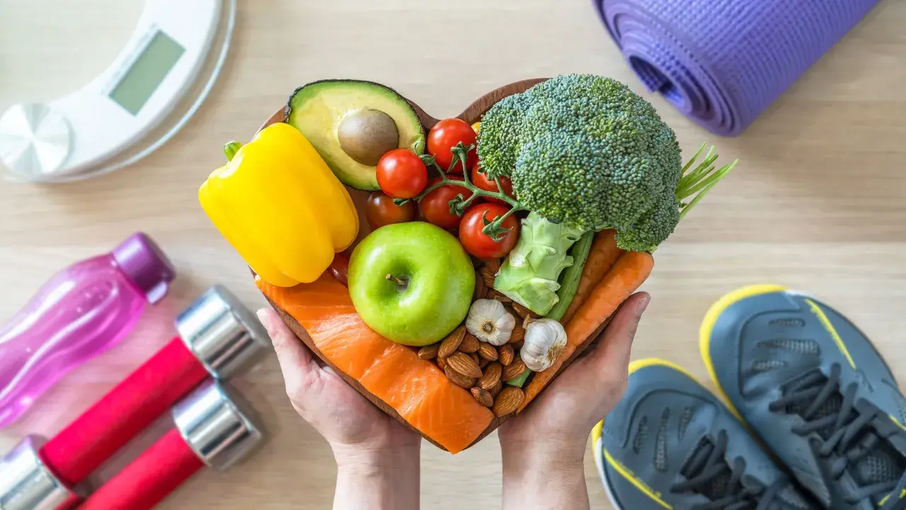 Mani che sorreggono un cuore di cibo sano: salmone, mela verde, avocado, verdure e frutta secca. Perfetto quando mangiare la mela per uno stile di vita attivo.