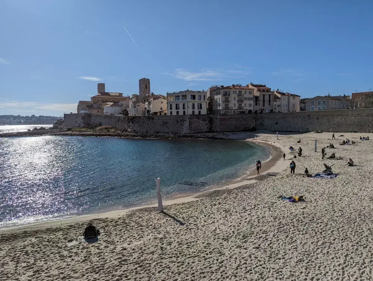 Sonniger nizza strand mit Menschen, die sich entspannen, und einer historischen Stadt im Hintergrund.