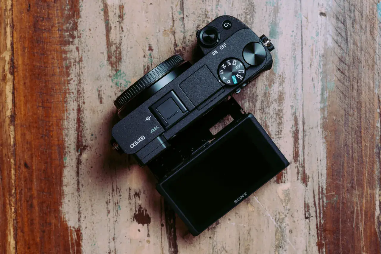 Czarny aparat Sony α6400 z uchylnym ekranem leży na drewnianym blacie. Idealny do testów i vlogowania.