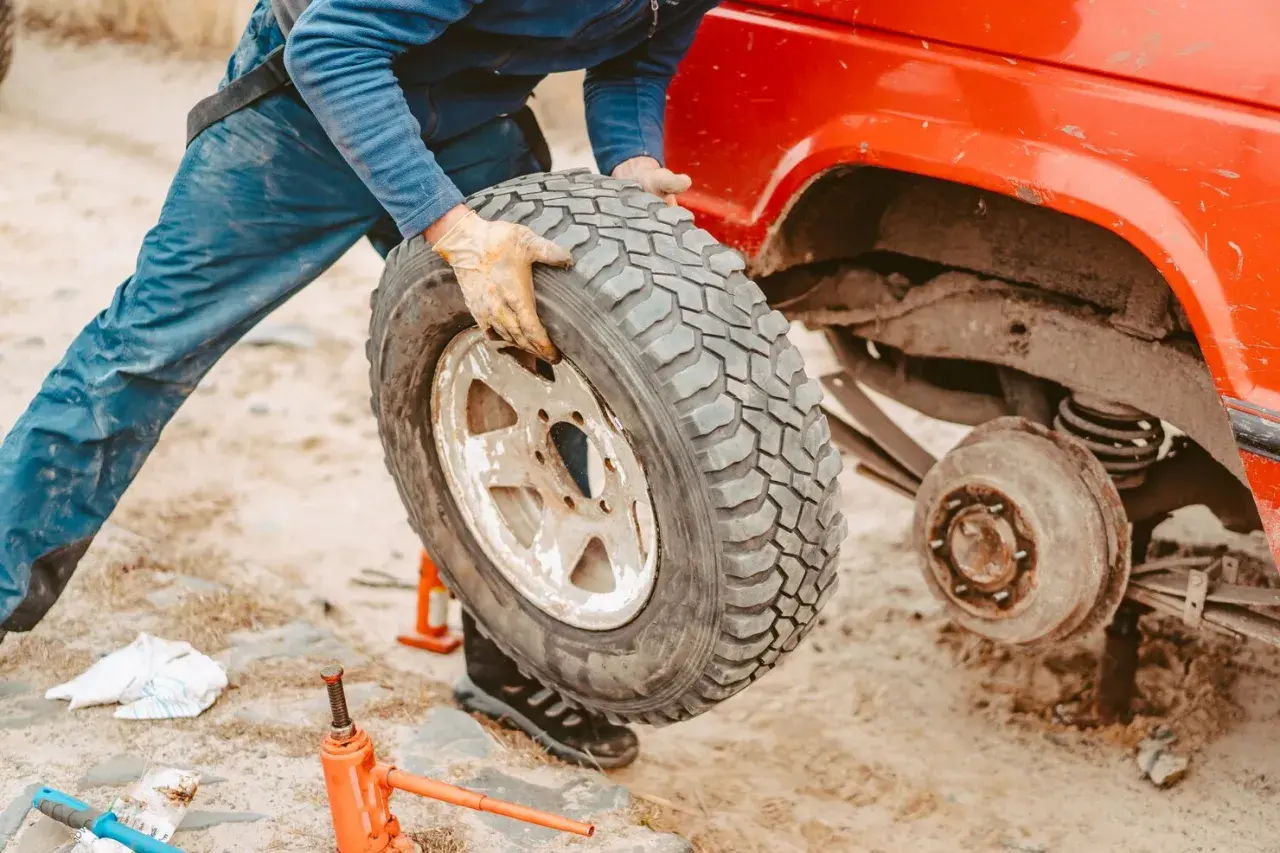 Persona con guanti smonta una gomma auto da un fuoristrada rosso. Si vede un cric arancione a terra, utile per capire dove smaltire gomme auto usate.