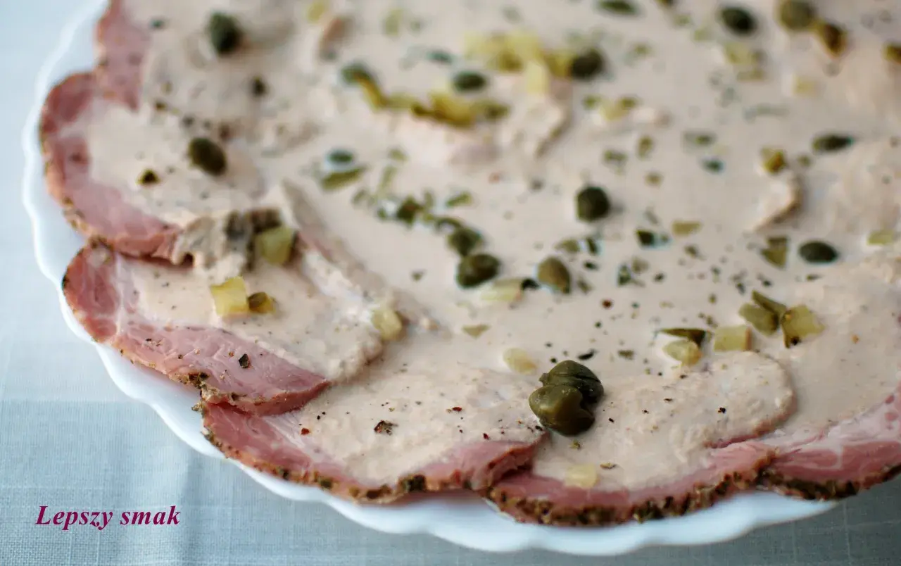 Cienkie plastry pieczonego mięsa wieprzowego polane kremowym sosem z kaparami i ziołami, klasyczne vitello tonnato.