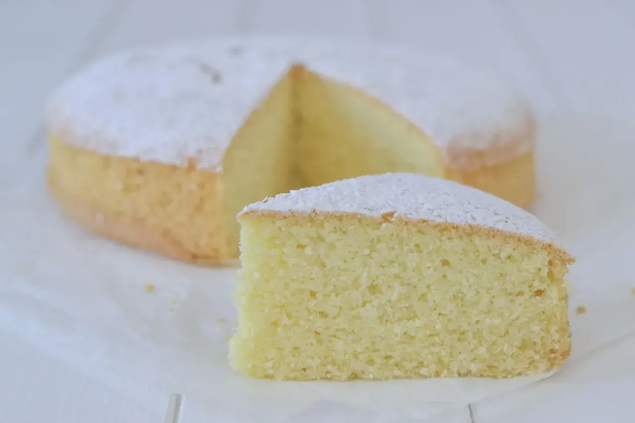 Una soffice torta con farina di riso, spolverata di zucchero a velo, con una fetta tagliata.