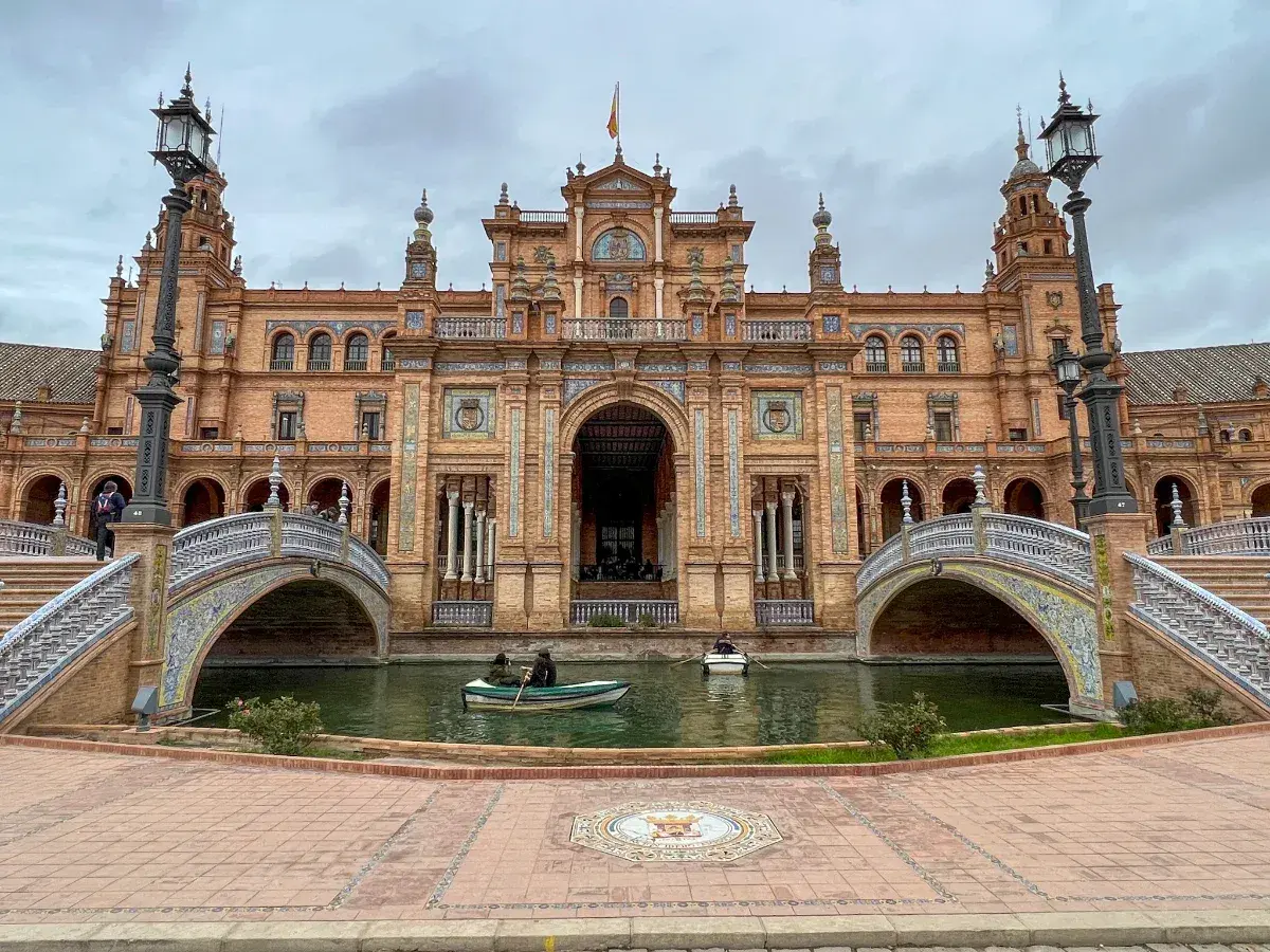 Majestatyczny plac hiszpański w Sewilli z kanałem i łódkami. Architektura zachwyca detalami.