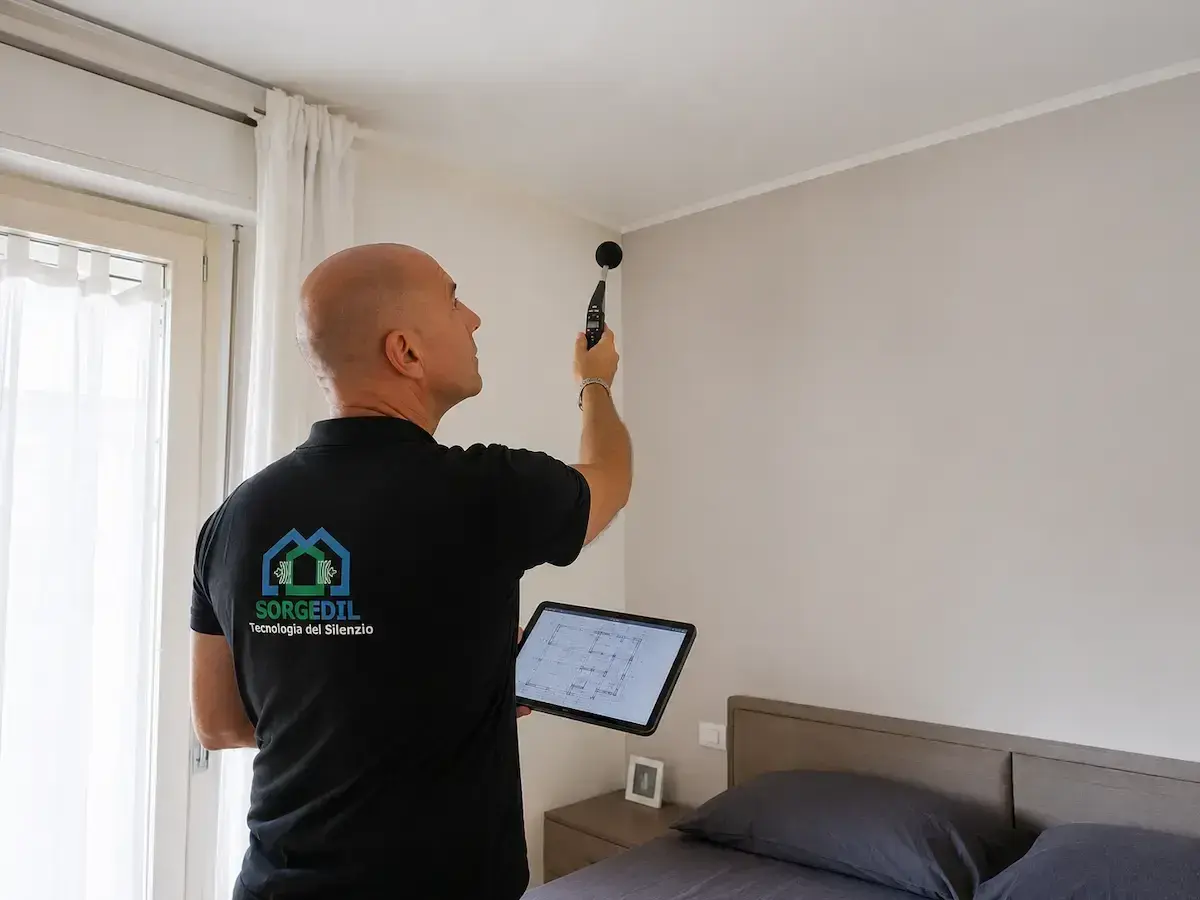 Tecnico con fonometro e tablet esegue una misurazione per la correzione acustica in una stanza da letto.