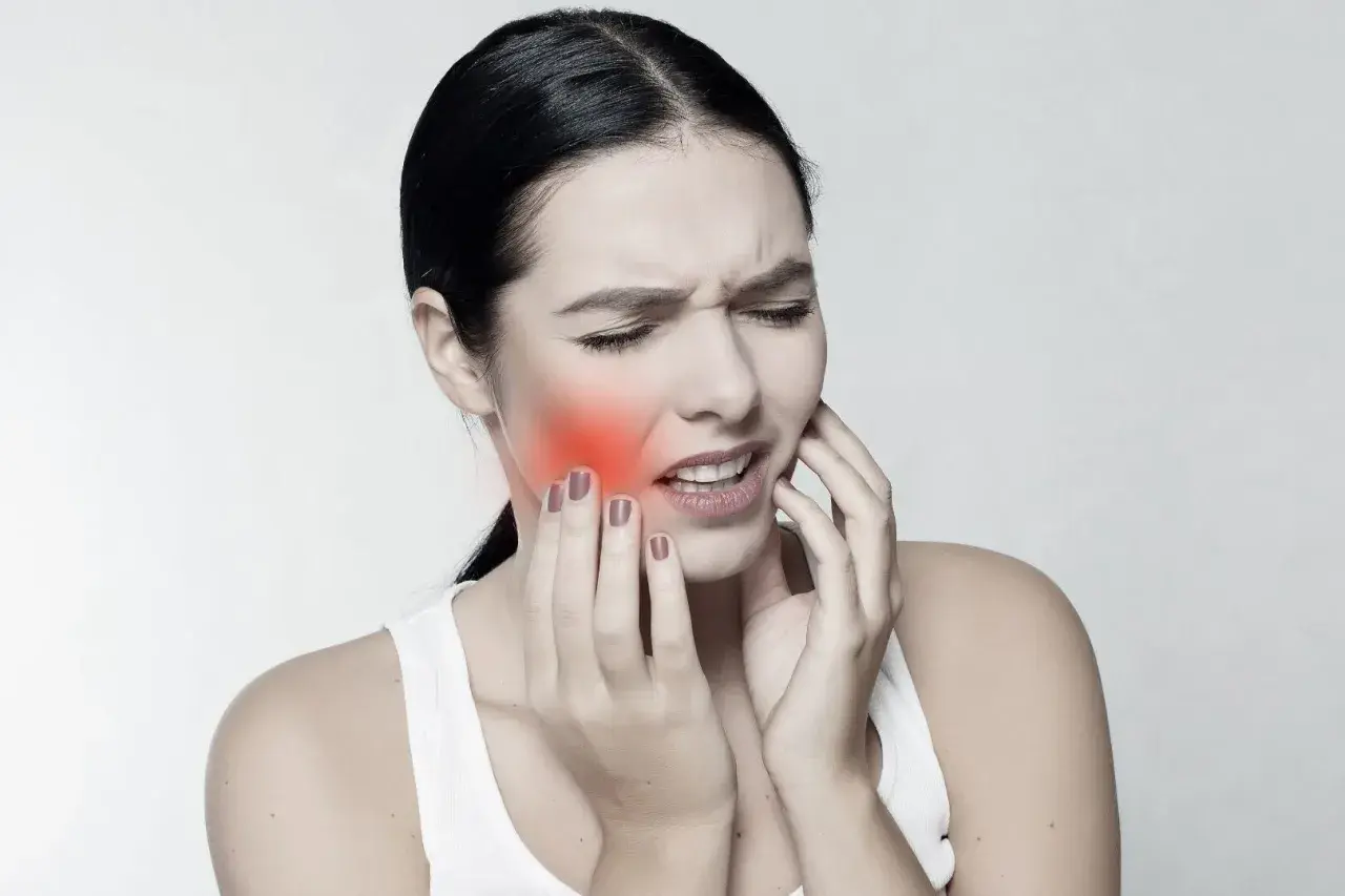 Mujer con dolor, tocándose la mejilla donde se ve un bulto mejilla interna enrojecido.