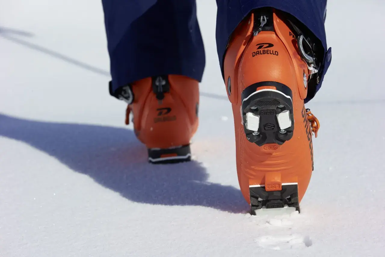 Botas de esquí naranjas Dalbello con suela de **grip walk** en la nieve, listas para la aventura.