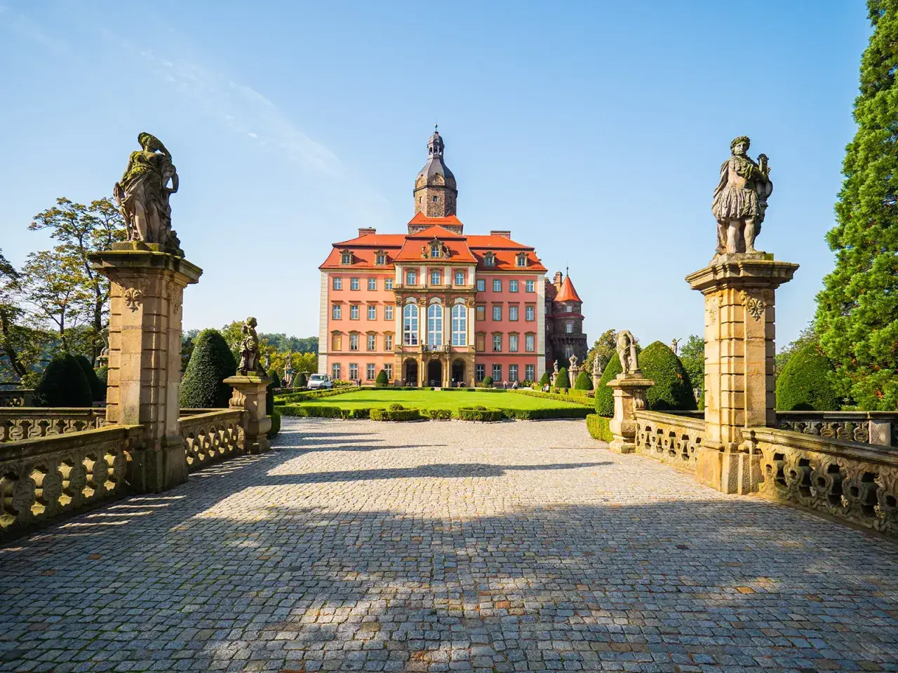 Zamek Książ z różową fasadą i wieżą, otoczony ogrodem. Poznaj zamek Książ ciekawostki i jego tajemnice.