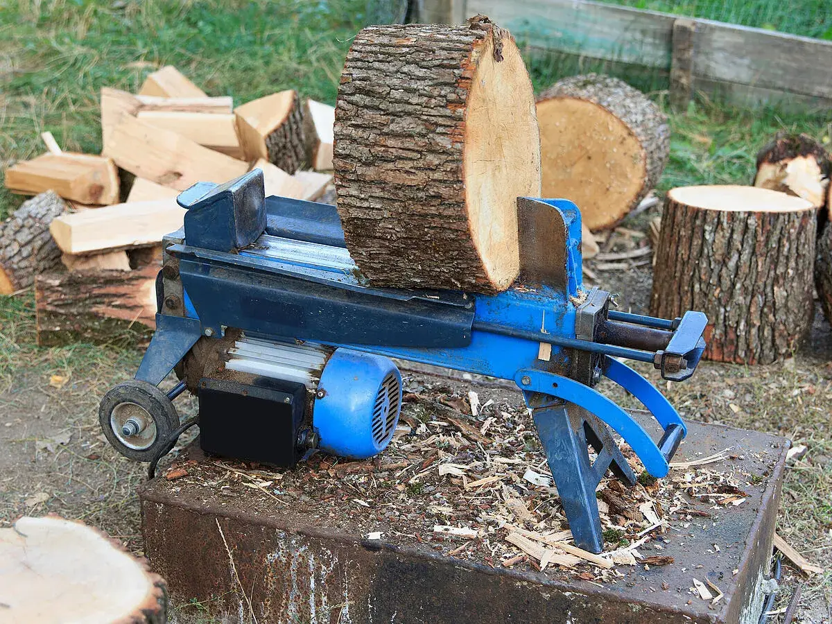 Ein Holzspalter mit einem dicken Holzstamm, bereit, dickes Holz zu spalten. Daneben liegen bereits gespaltene Holzscheite.