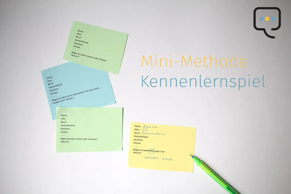 Bunte Zettel mit Fragen für ein Kennenlernspiel liegen auf weißem Grund. Ein grüner Stift liegt daneben.