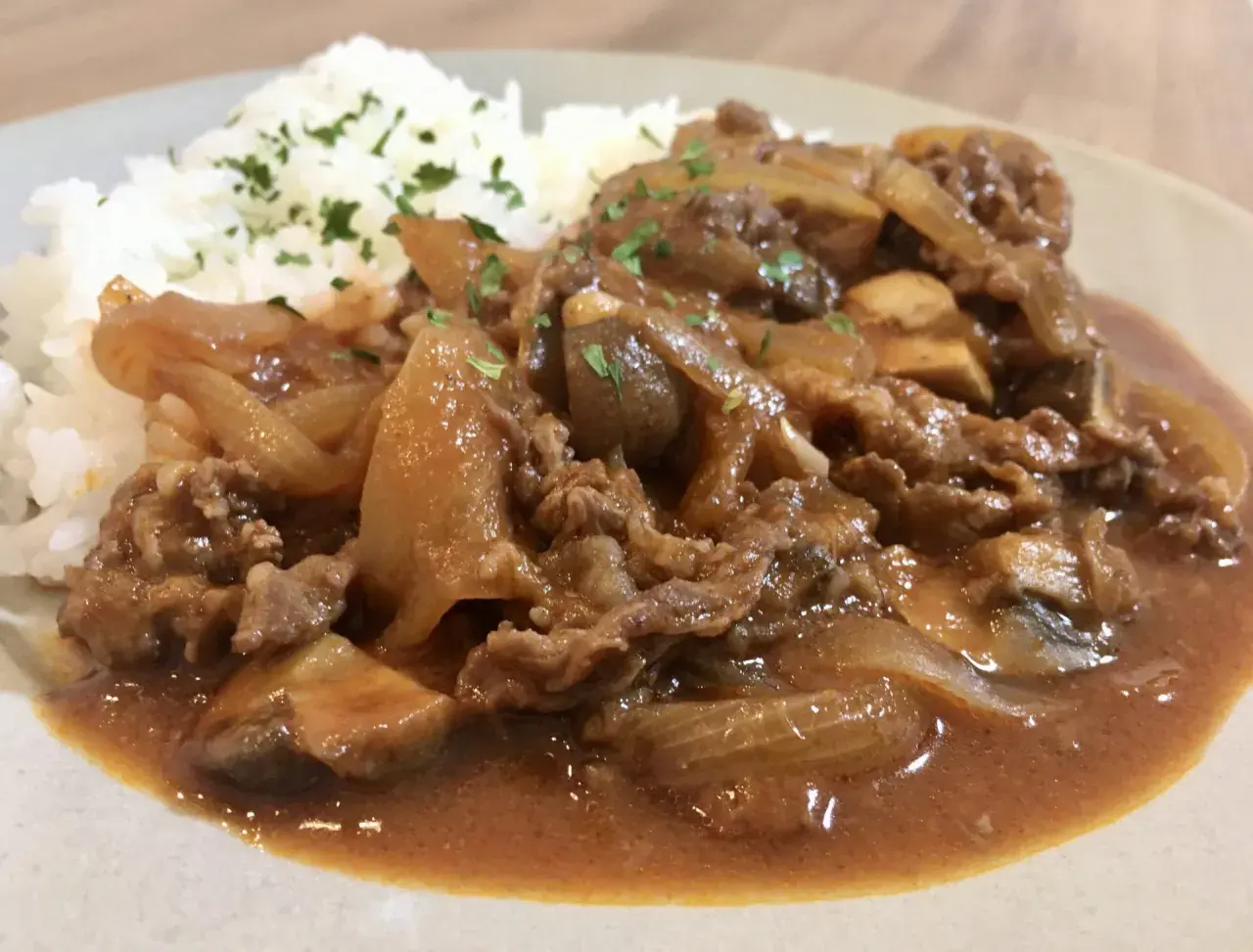 A plate of Hayashi Rice, featuring tender beef and onions in a rich demi-glace sauce served over fluffy white rice, garnished with parsley.