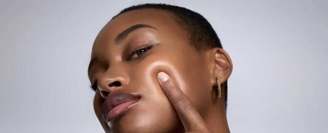 Piel oscura con un brillo dewy, resaltando sus pómulos y labios.