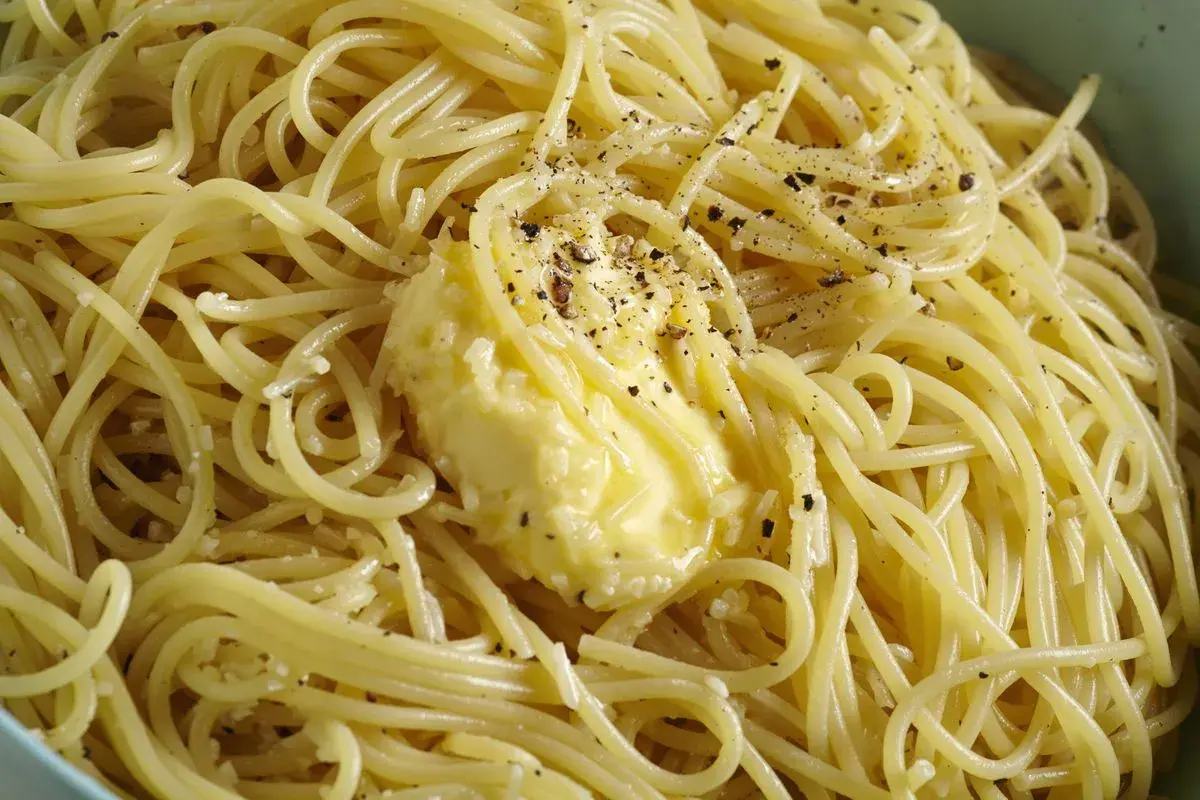 Un piatto di spaghetti fumanti, conditi con burro fuso e pepe nero macinato, pronti per essere gustati come un classico cacio e pepe.