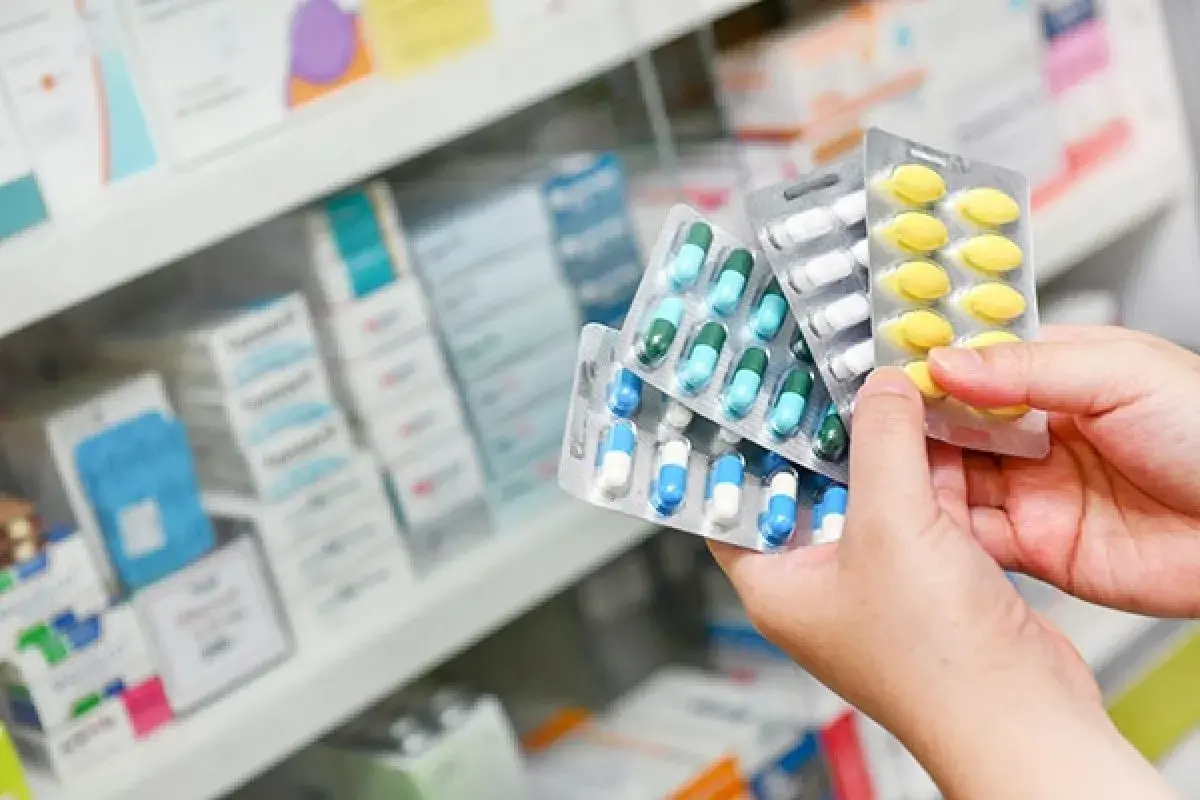 Manos sostienen blísteres de pastillas, eligiendo entre paracetamol o ibuprofeno.