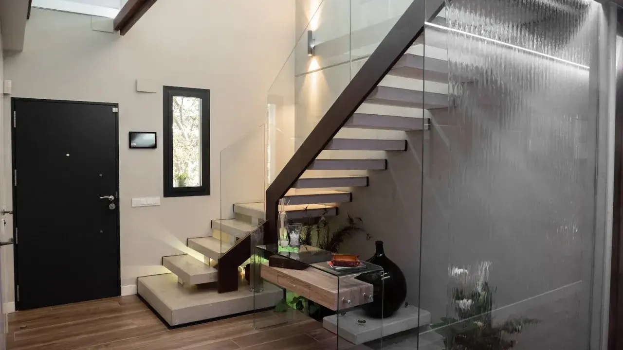 Modernas escaleras interiores prefabricadas con peldaños flotantes de hormigón y barandilla de cristal. Una cascada interior ilumina el espacio.