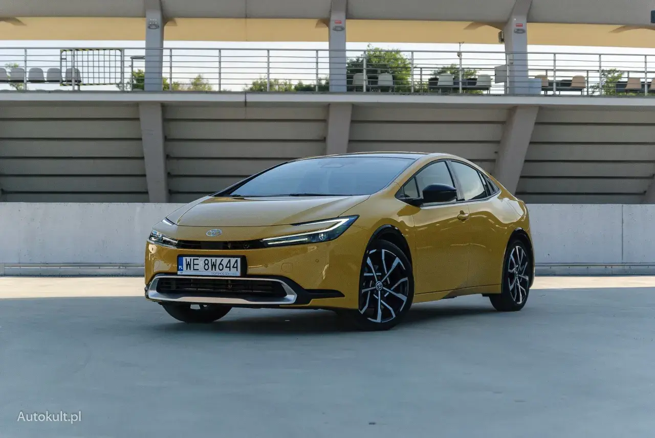Nowy żółty Toyota Prius z nowoczesnym designem stoi na betonowym placu przed trybunami stadionu.