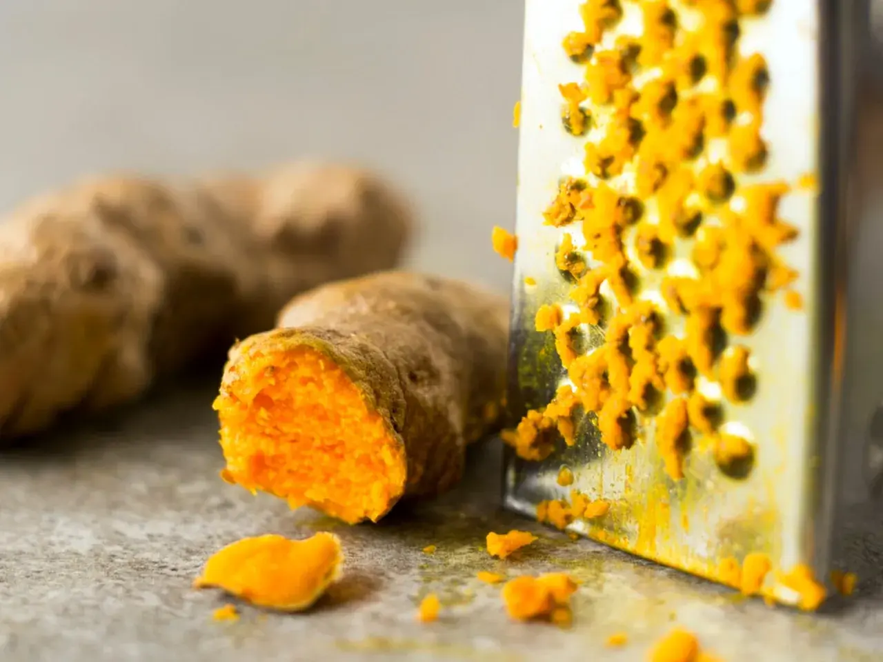 Frisch geriebene Kurkuma auf einem Metallreibe. So lässt sich die leuchtend orangefarbene Wurzel für die Lagerung vorbereiten.