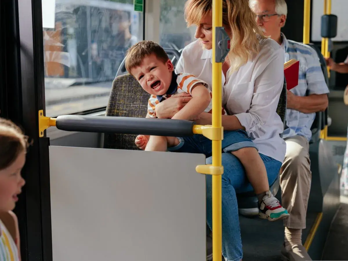 Płaczące dziecko na rękach matki w autobusie, obok siedzi starszy mężczyzna.