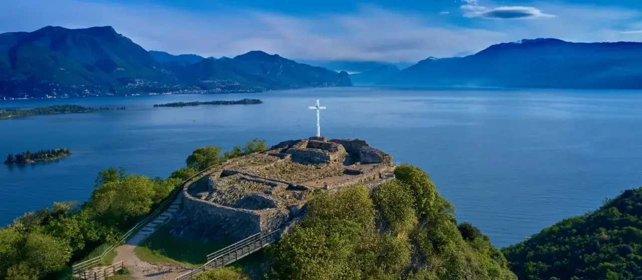Rovine di un castello con una croce bianca su una collina a Manerba del Garda. Vista panoramica sul Lago di Garda e le montagne.