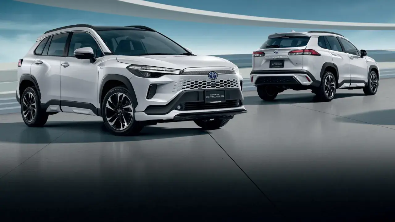 Dwa białe SUV-y Toyota Corolla Cross 2025 stoją na betonowej podłodze, jeden z przodu, drugi z tyłu.