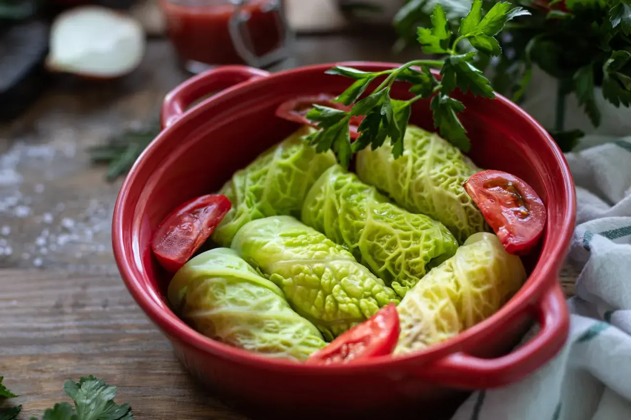 Choux verts au four prêts à cuire, garnissent un plat rouge avec des tomates et du persil frais.