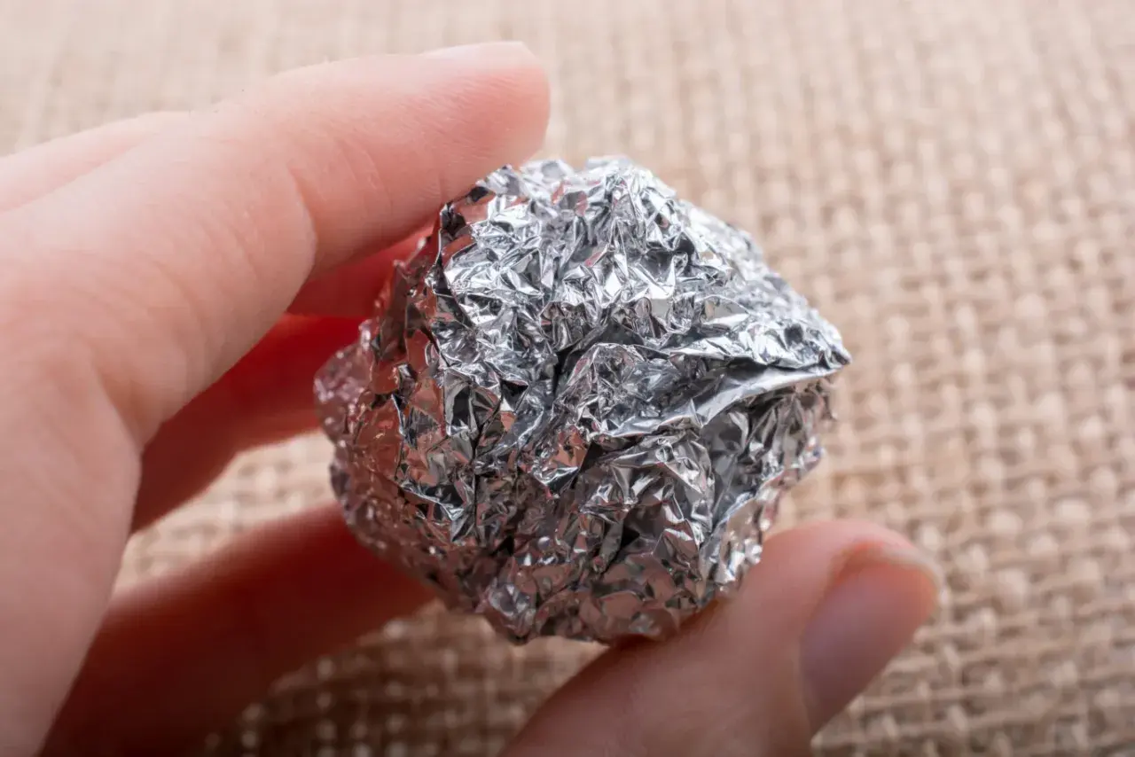 Dłoń trzyma kulkę z pogniecionej folii aluminiowej, która może być szkodliwa.