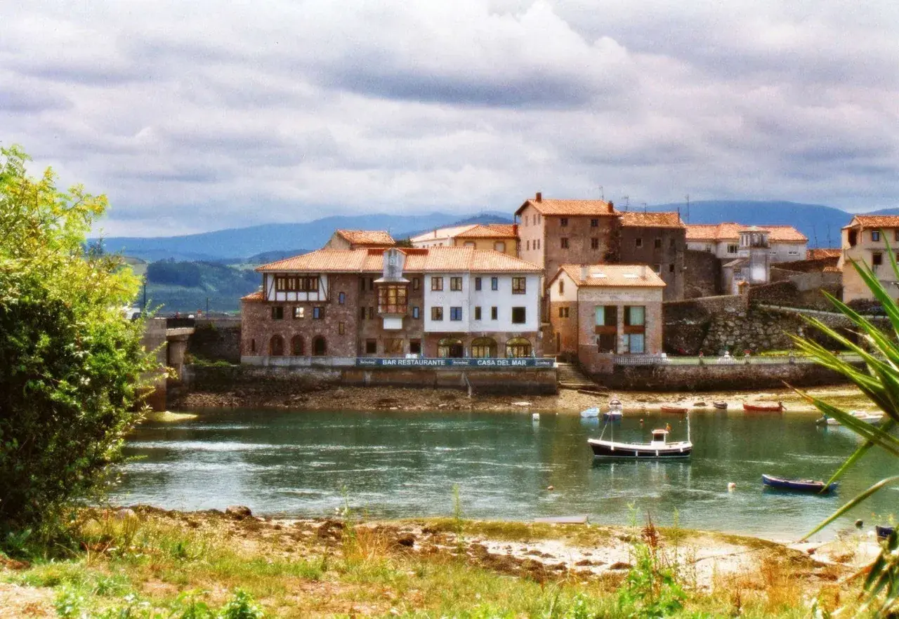 Pueblos de Cantabria con playa, casas de piedra y tejados rojos junto a un río tranquilo con barcas.