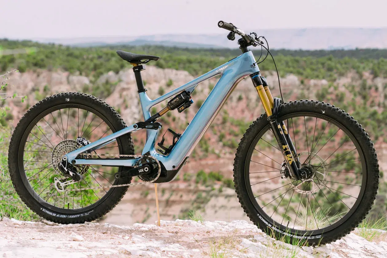 A light blue specialized levo 4 electric mountain bike is parked on a rocky trail with a scenic canyon in the background.